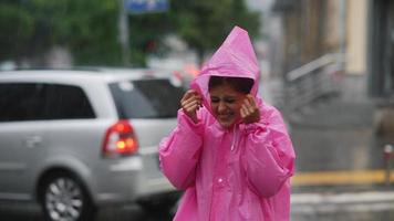 mulher de poncho com capuz rosa fica e ri na rua da cidade na chuva video