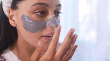 Young beautiful woman applies mask on nose and cheeks video