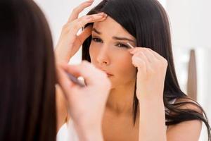 Tweezing eyebrows. Concentrated young woman tweezing eyebrows while looking at the mirror photo