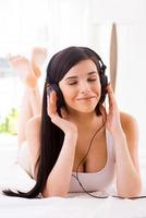 Enjoying music in bed. Beautiful young smiling woman adjusting her headphones while listening to the MP3 player in bed photo