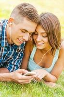 Enjoying music together. Young couple lying on the grass and choosing music on the phone photo