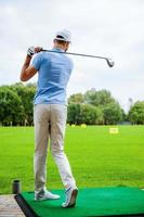 Teeing off. Full length rear view of young male golfer playing golf photo