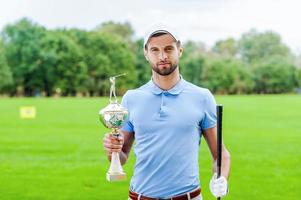 Confident winner. Confident golfer holding golf ball and driver while standing on golf course and looking over shoulder photo