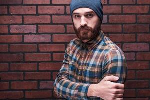 Bearded handsome. Handsome young bearded man looking at camera while standing against brick wall photo