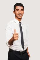 Confident young Afro-American man in formalwear stretching out hand with thumb up while standing against grey background photo