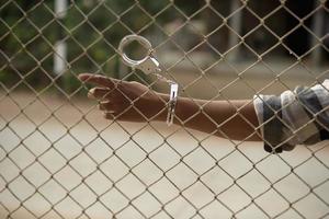 close-up photo of hands in prison steel mesh handle Handles the steel mesh cage, lacks independence.