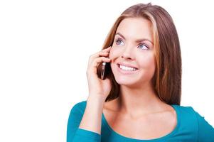 Communication in pleasure. Beautiful young women talking on the mobile phone and smiling while standing against white background photo