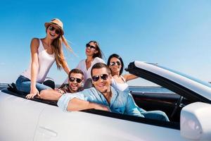 We love spending time together Group of young happy people enjoying road trip in their white convertible and smiling at camera photo