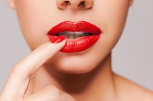 Passion lips. Close-up of a beautiful women holding finger on her red lips while standing against grey background photo