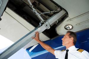 Checking the wing. Low angle view of confident male pilot in uniform examining airplane wing photo