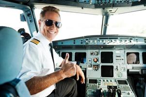 listo para volar. vista trasera de un piloto masculino confiado que muestra su pulgar hacia arriba y sonríe mientras está sentado en la cabina foto