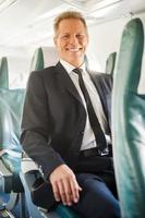Ready to flight. Confident mature businessman sitting at his seat in airplane and smiling photo