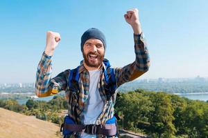 I have made it Happy young man carrying backpack and looking at camera with raising arms photo