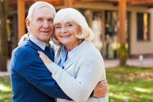 Love forever. Happy senior couple bonding to each other and smiling while standing outdoors and in front of their house photo