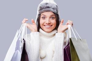 Shopping in any weather . Happy young women wearing warm winter clothing and holding packages with purchases while standing against grey background photo