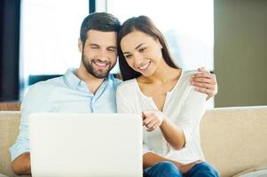 Surfing the net together. Beautiful young loving couple sitting together on the couch and looking at laptop photo