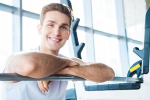 Taking a break after workout. Handsome young man keeping arms crossed and looking at camera while sitting at the bench press photo