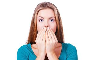 Oops Surprised young woman covering mouth with hands and staring at camera while standing isolated on white photo