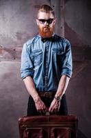 Stylishly confident. Handsome young bearded man in sunglasses looking at camera while holding a suitcase in his hands photo