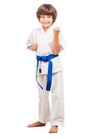 I can defence myself. Full length of little boy in karate uniform standing in karate position while isolated on white photo