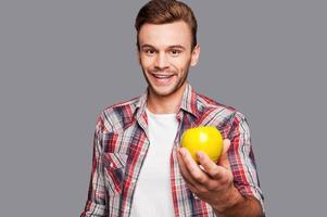 Healthy alternative. Smiling man holding green apple in front of him while standing against grey background photo