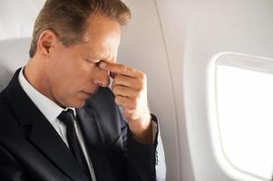 Feeling that awful headache. Frustrated mature businessman touching his face with hand and keeping eyes closed while sitting at his seat in airplane photo