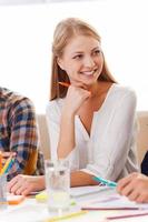 Working with pleasure. Confident young woman in smart casual wear looking away and smiling while sitting at her working place photo