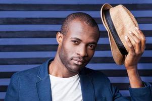 Well hello Handsome young African man holding his hat and looking at camera while standing against striped background photo