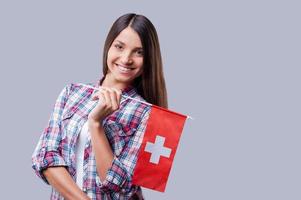 Beauty with Swiss flag.  Happy young women holding flag of Switzerland while standing against grey background photo