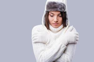 sintiéndose helado. mujeres jóvenes congeladas en ropa de invierno abrazándose a sí mismas mientras están de pie contra un fondo gris foto
