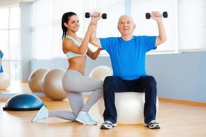 Weight exercises. Confident female physical therapist working with senior man in health club photo