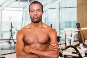 Strong and confident. Confident young African man keeping arms crossed and looking at camera while standing in gym photo