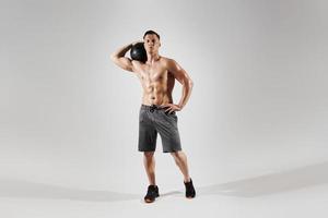 hombre joven en forma que lleva una pelota medicinal en el hombro mientras está de pie contra el fondo blanco foto