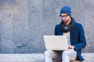 navegar por la red al aire libre. un joven apuesto con ropa informal elegante que trabaja en una laptop mientras se sienta al aire libre foto