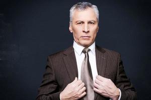 Portrait of success. Portrait of confident senior man in formalwear looking at camera and adjusting his jacket while standing against blackboard photo