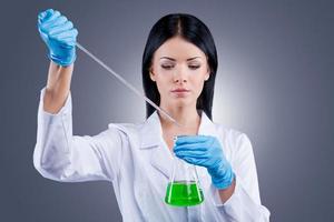 Trying to heal the world. Beautiful female doctor in white uniform holding flasks while standing against grey background photo