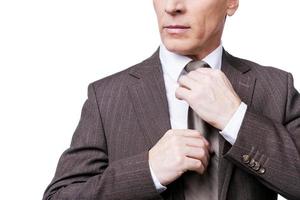 Style and success. Cropped image of confident mature man in formalwear adjusting his necktie while standing against white background photo