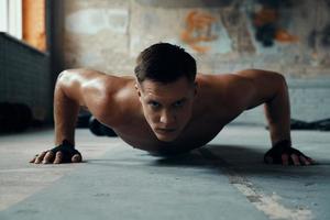 Confident young man looking at camera while doing push-up exercises in gym photo