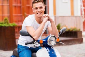 Proud of his new scooter. Handsome young man sitting on scooter and smiling photo