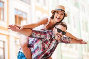 Happy loving couple. Happy young man piggybacking his girlfriend while keeping arms outstretched photo