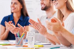 Good job Cropped image of happy business people in smart casual wear sitting together at the table and applauding to someone photo