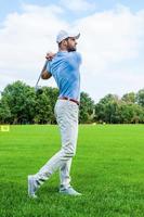 gran golpe longitud total de golfista confiado balanceando a su conductor y mirando hacia otro lado mientras está de pie en el campo de golf foto