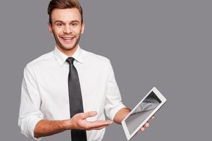 Keep up with technological progress. Cheerful young man holding a digital tablet and pointing it while standing against grey background photo