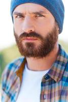 Brutal look. Portrait of handsome bearded man looking at camera while standing outdoors photo