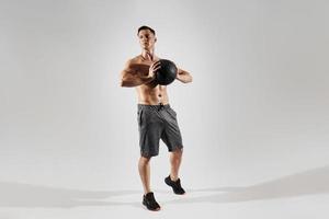 Handsome young man with perfect body holding medicine ball against white background photo