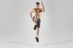 Confident fit man with perfect body running against white background photo