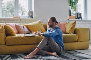 Relaxed young man using laptop while sitting on the floor at home photo