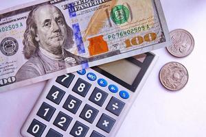 la calculadora y los billetes de dólar se colocan sobre una mesa blanca. foto