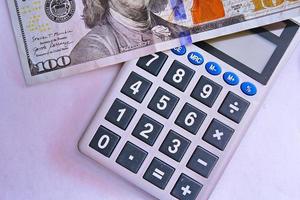 Calculator and dollar bills are placed on a white table. photo