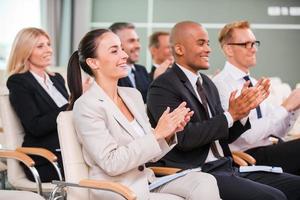 Applauding to speaker. Group of happy business people in formalwear sitting at the chairs in conference hall and applauding photo